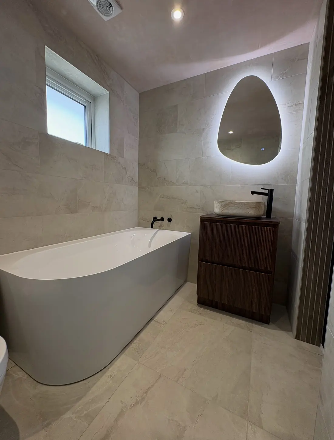 Freestanding corner bath with a dark walnut vanity and an egg-shaped backlit mirror