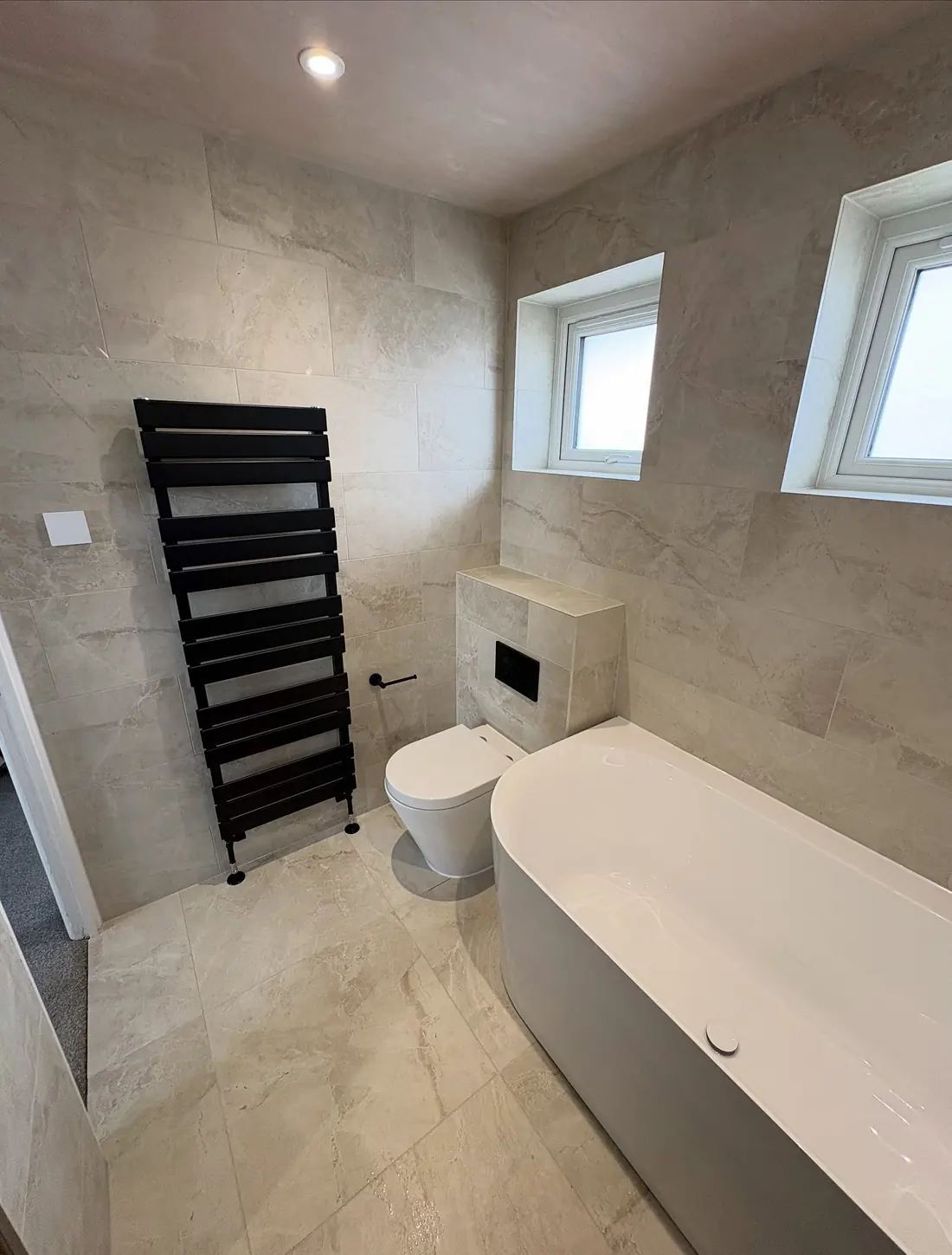 Matt black towel rail beside a wall-hung toilet and a freestanding bath