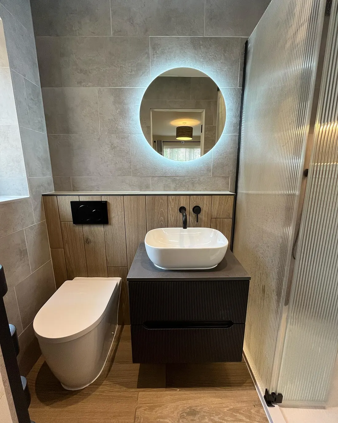 En-suite with a round backlit mirror, a black wall-mounted tap and a floating vanity with a vessel basin