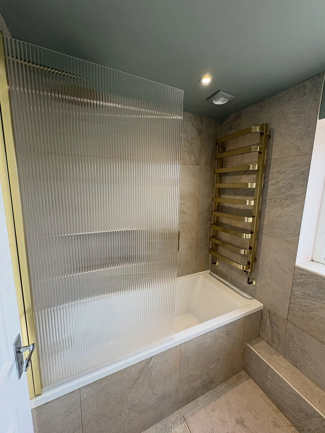 Bath with a full-height fluted glass screen and a brass heated towel rail