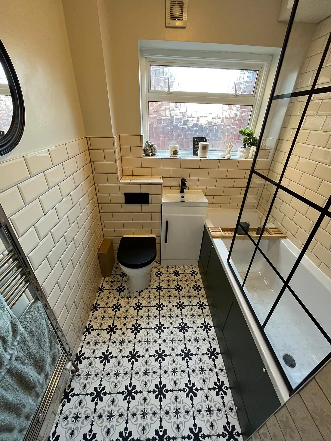 Cream metro-tiled bath with a black grid-framed shower screen and a patterned floor