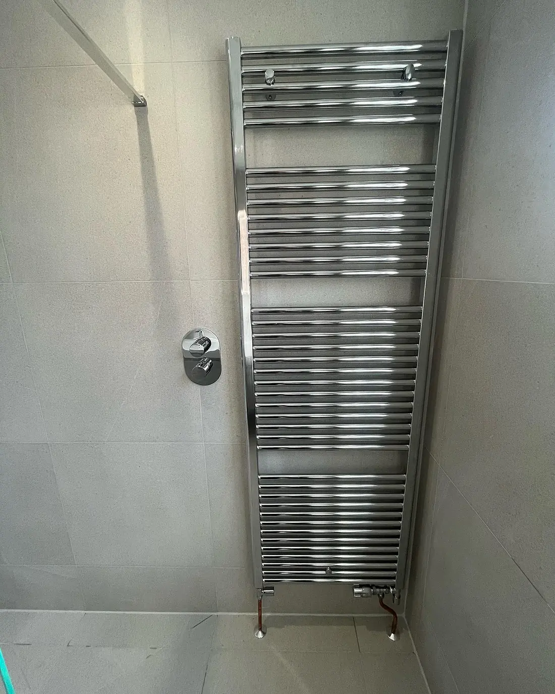 Tall chrome heated towel rail on a grey tiled wall