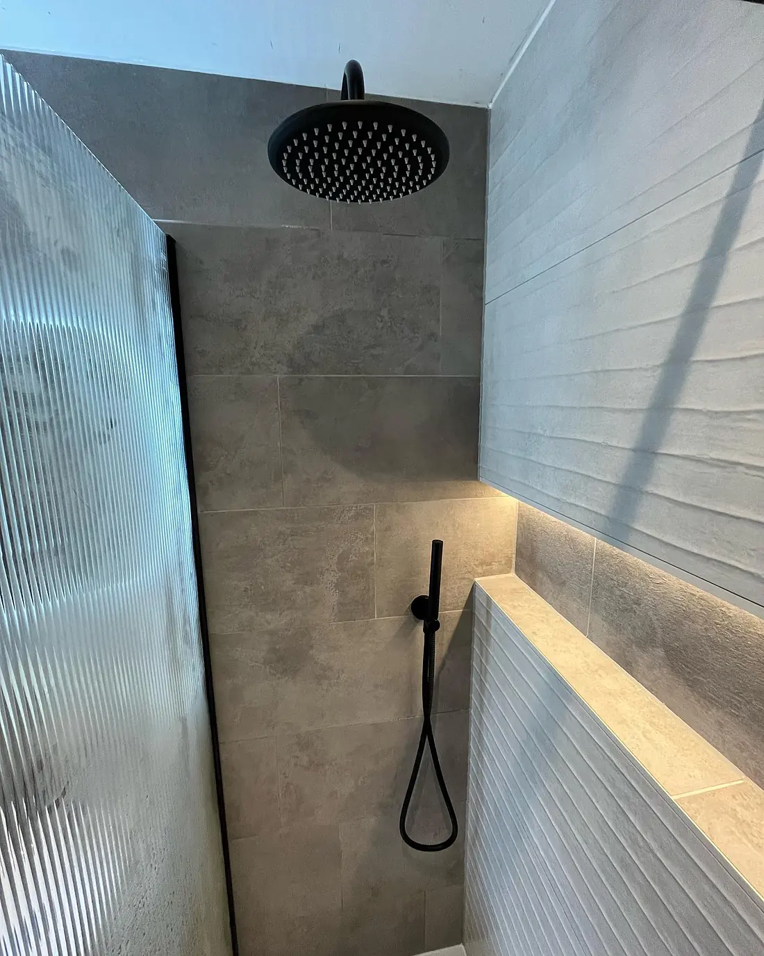 Black rain shower head behind a fluted glass screen