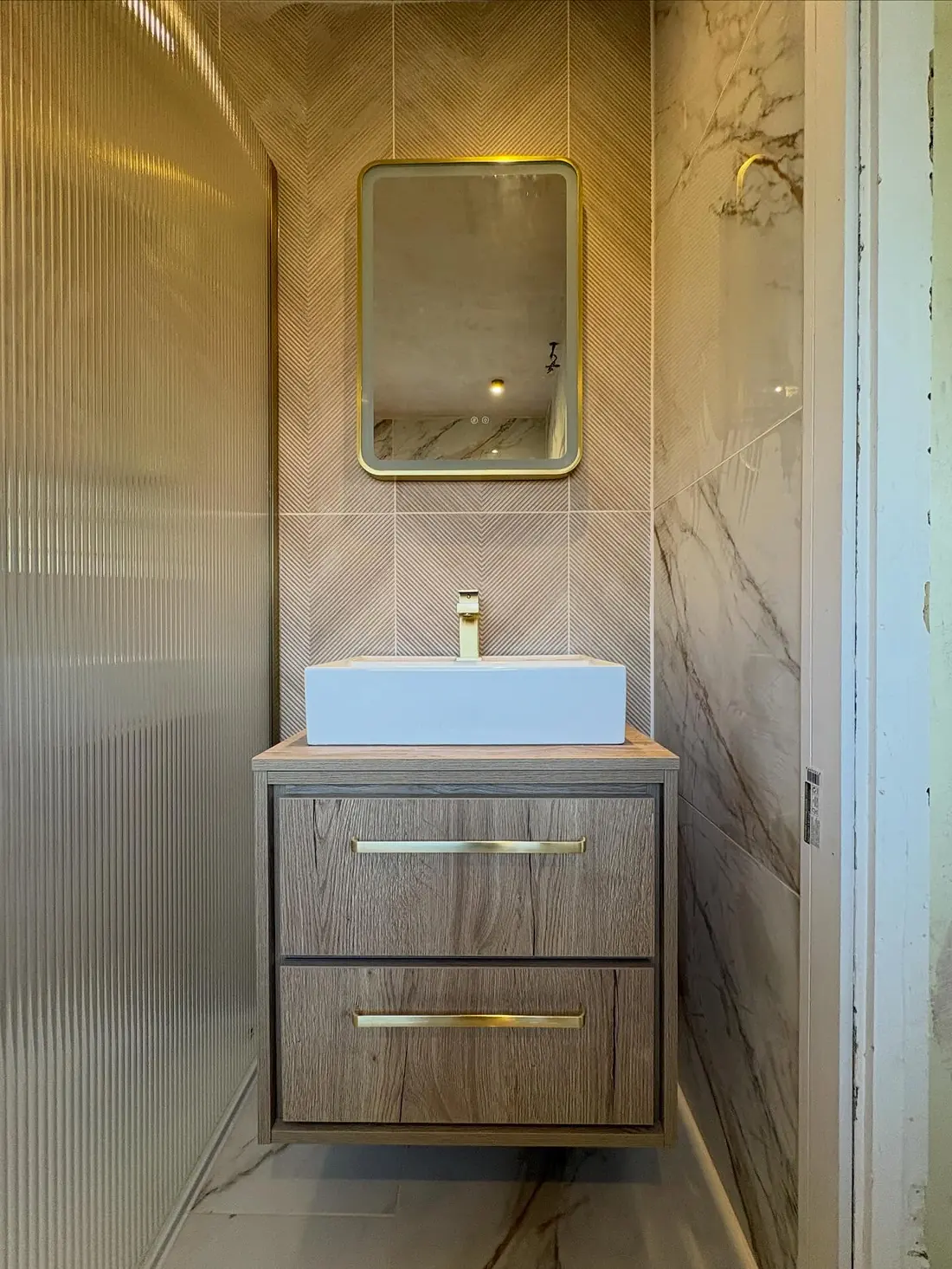 Oak wall-hung vanity with a vessel basin and a brass-framed mirror against herringbone tiles