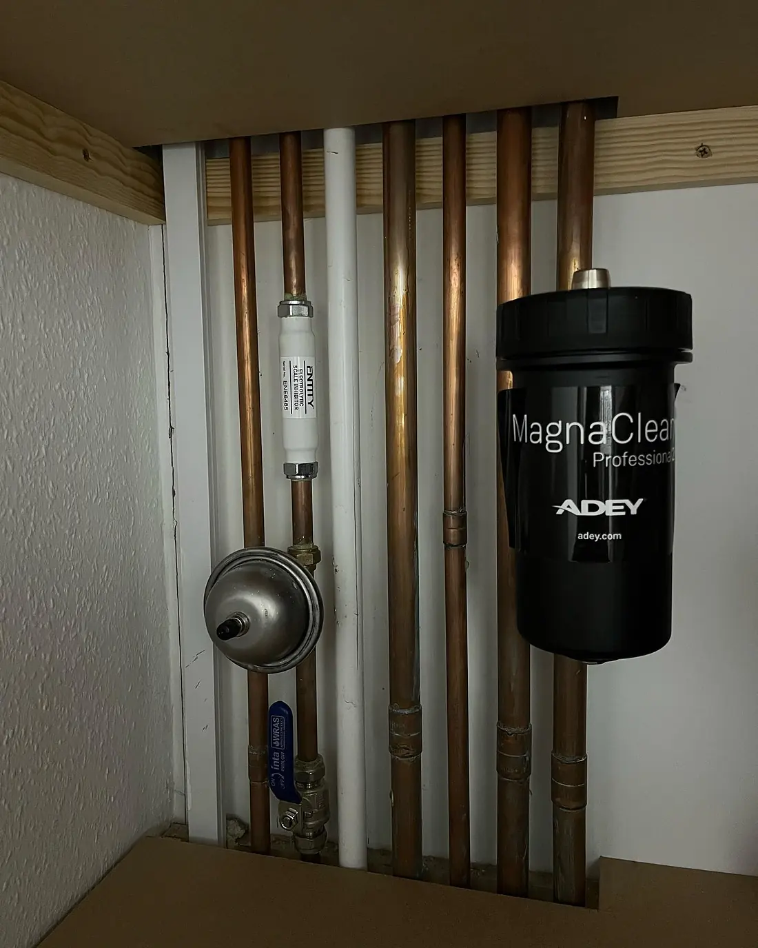 Copper and white pipework in a boiler cupboard with a black magnetic filter