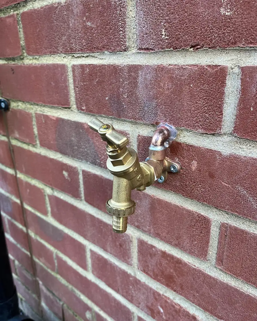 A brass outside tap on a red brick wall