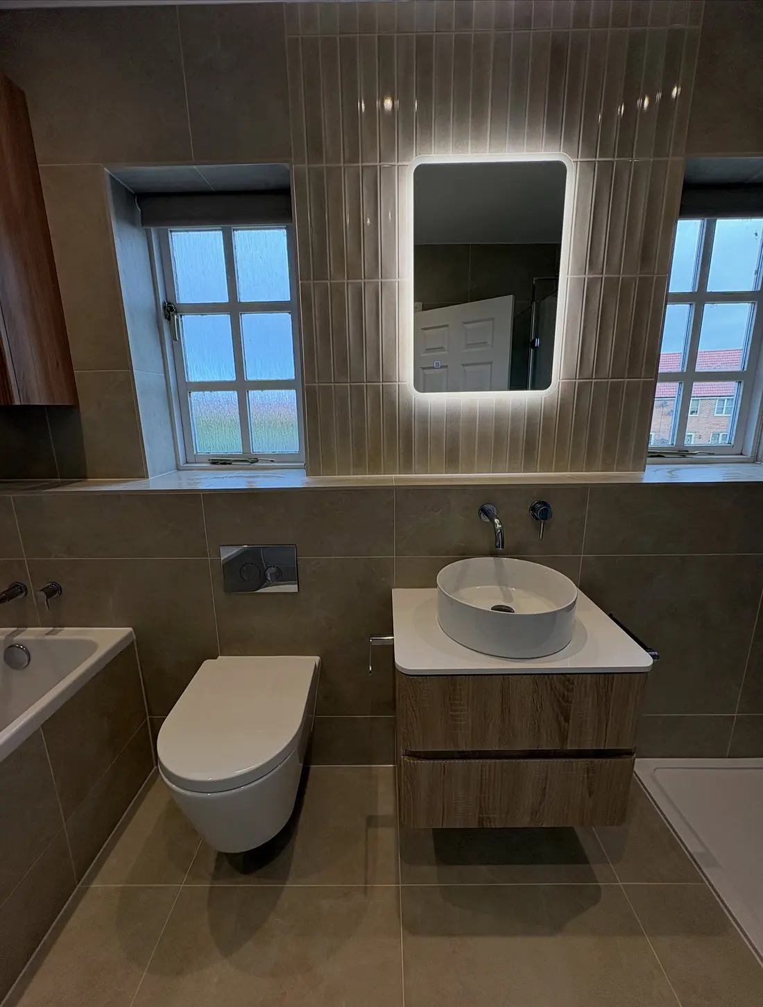 Beige bathroom with a wall-hung toilet, a vanity with a round basin and a backlit mirror