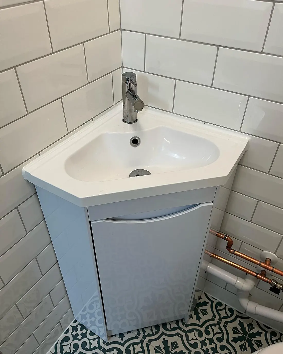 Corner basin on a small cloakroom vanity with white metro tiles and a patterned floor