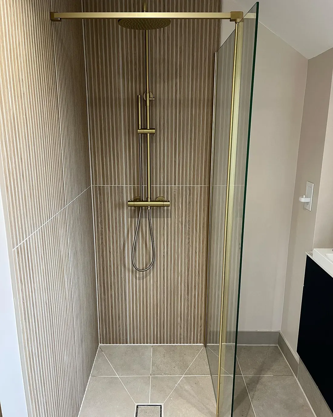 The finished shower with fluted tiles, a brass thermostatic shower and a glass screen