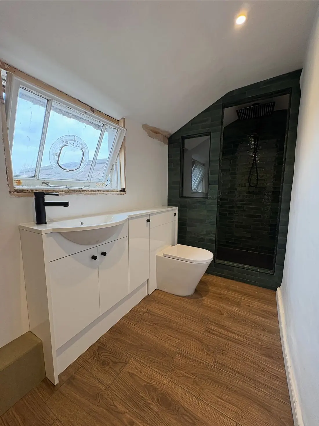 After: a new bathroom with an oak-effect floor, white basin units and a black tap, with the green-tiled shower beyond